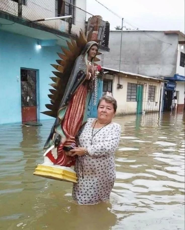 Woman wading through floodwater carrying a Virgen de Guadalupe statue